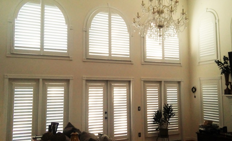 Television room in open concept Gainesville home with plantation shutters on high windows.